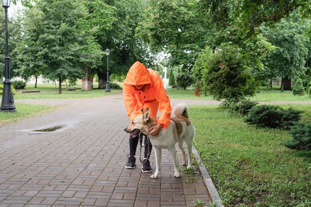 Young woman in orange raincoat walking with her dog in a park