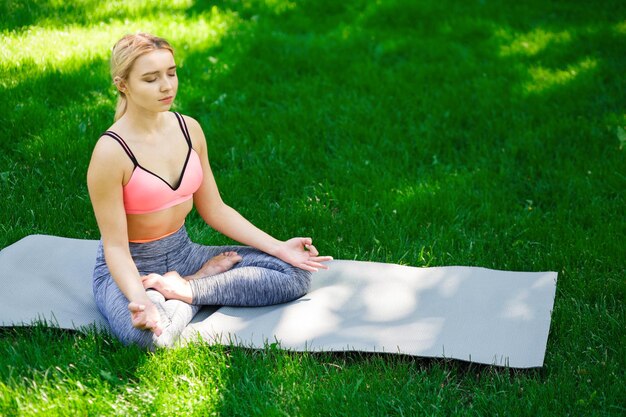 Young woman outdoors, meditation exercises. Girl does lotus pose for relaxation. Wellness, calmness, relax, healthy, active lifestyle concept