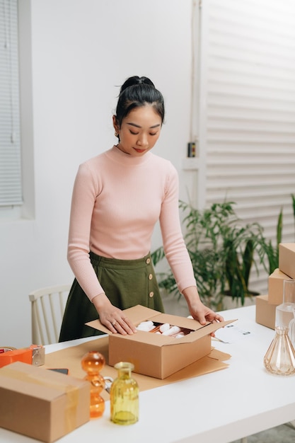 Young woman owener of small business packing product in boxes preparing it for delivery