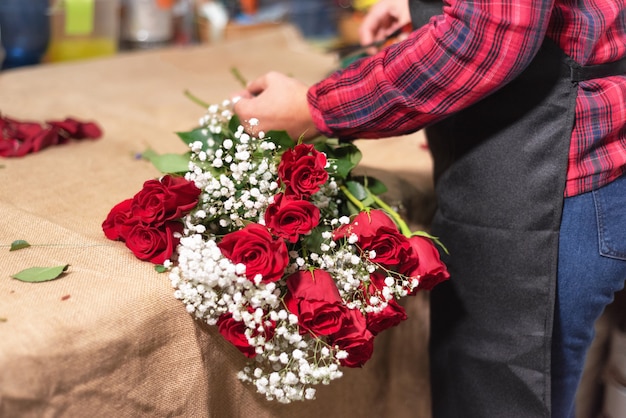 Young woman owner of florist shop arranging bouquet of roses.