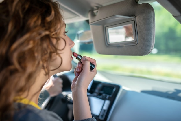 Young woman painting lips in a car