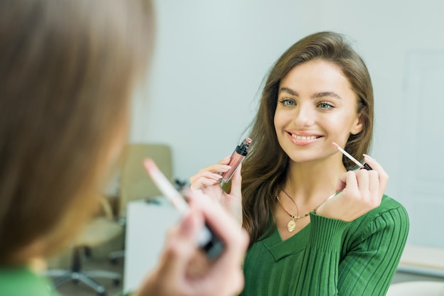 Young woman paints lips in beige