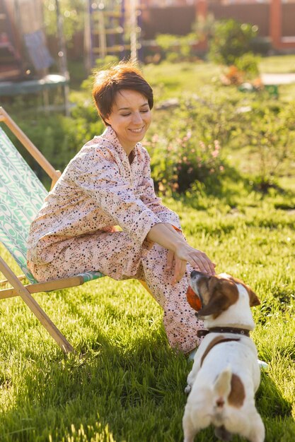 Young woman in pajama is resting in chair on a green lawn on sunny summer day village and country life