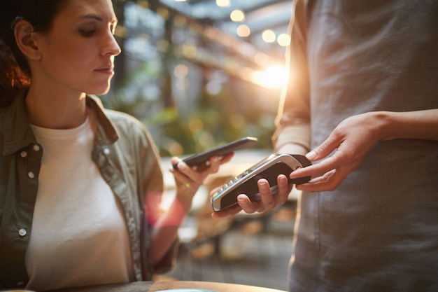 Young Woman Paying via Smartphone in Cafe