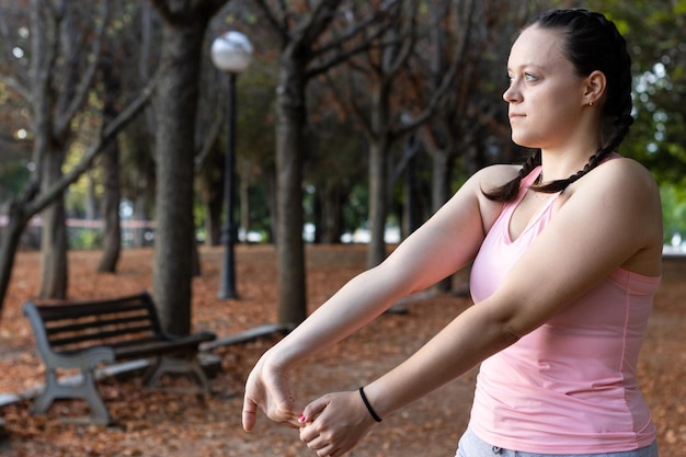 Young woman performing biceps stretches after playing sports in autumn in the street