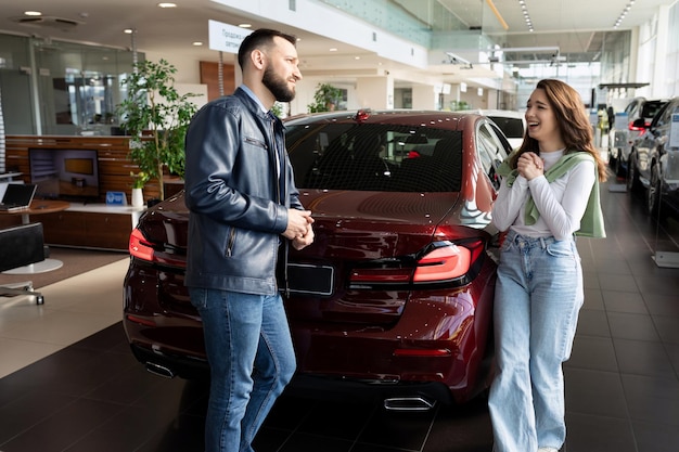 A young woman persuades her man in a car dealership to buy her a new car