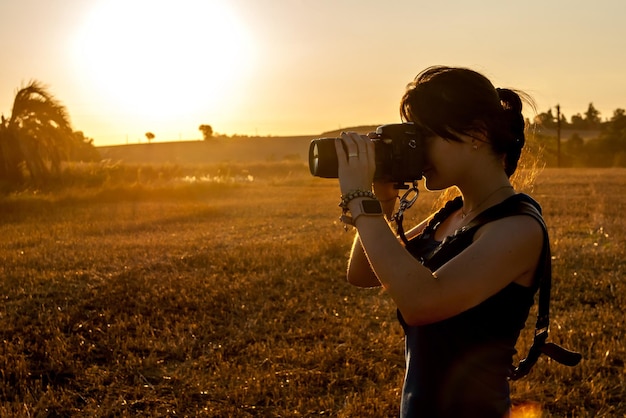 Young woman photographing in a soybean field at sunset