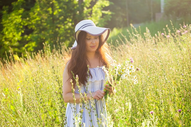 Photo young woman picking flowers in the meadow in summer evening