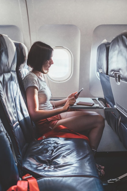 Young woman on a plane with a smartphone in her hands