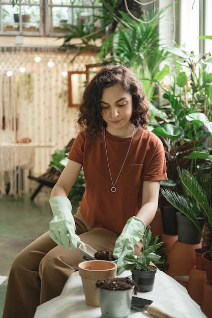 Young woman planting green plant in pots while sitting in the garden