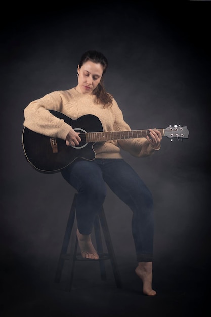 Young woman playing acoustic guitar with smoke and black background