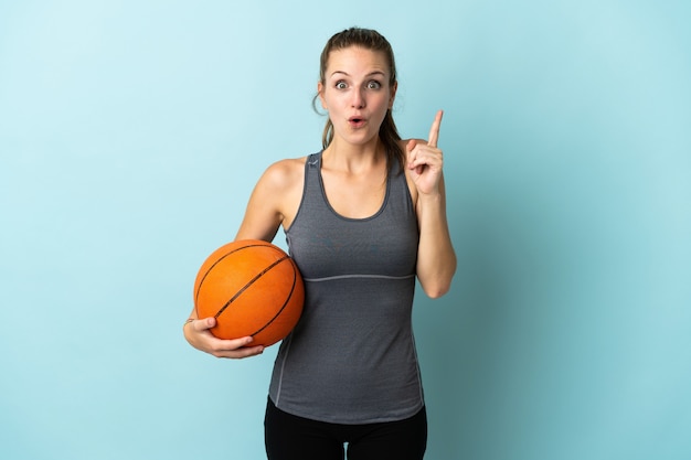 Young woman playing basketball isolated on blue background intending to realizes the solution while lifting a finger up