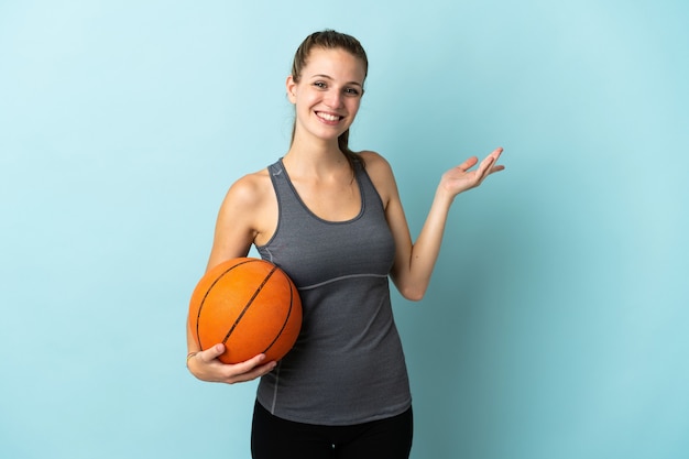 Young woman playing basketball isolated on blue extending hands to the side for inviting to come