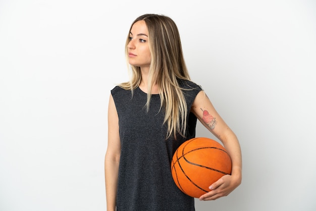 Young woman playing basketball over isolated white wall looking to the side