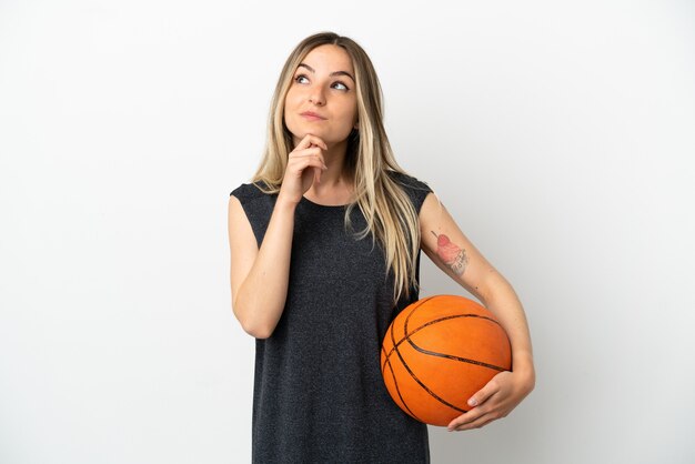 Young woman playing basketball over isolated white wall and looking up