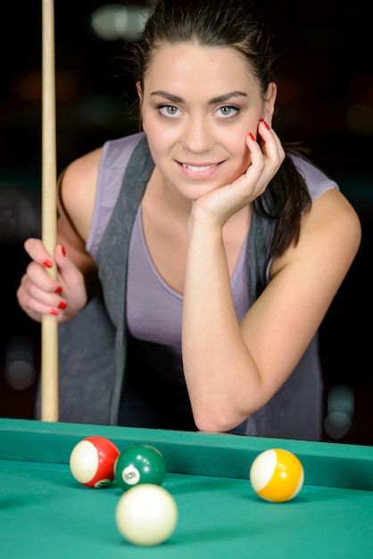 Young woman playing billiards in the dark billiard club