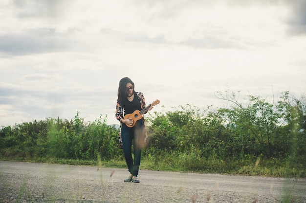 Young woman playing on brown Ukulele in the park.