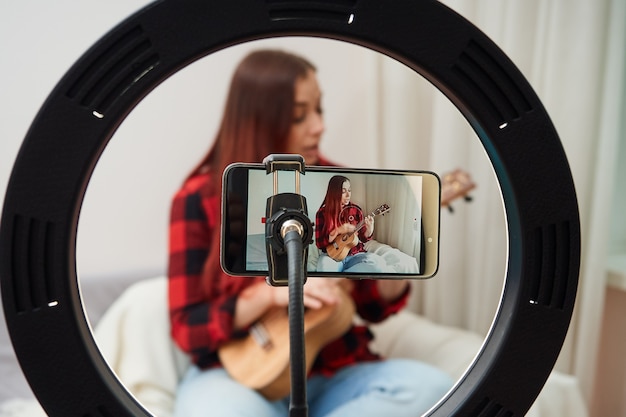 Young woman plays the ukulele records on the phone camera the musician performs a live concert from home