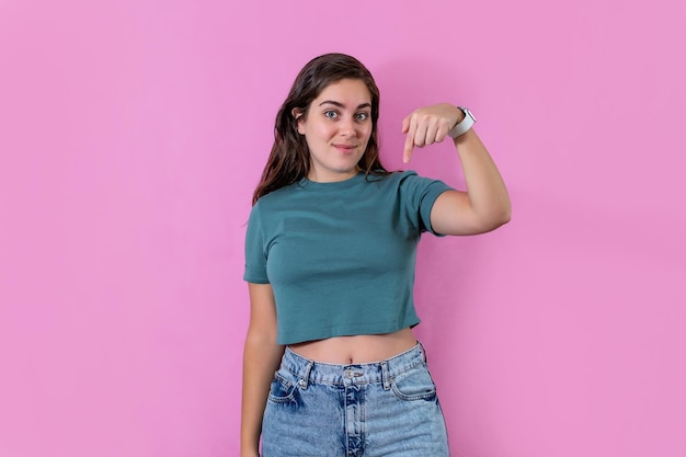 Young woman pointing downward and looking at camera on pink banner background with copy space