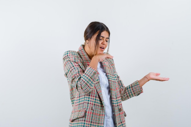 Young woman pointing something with opened palms on white background