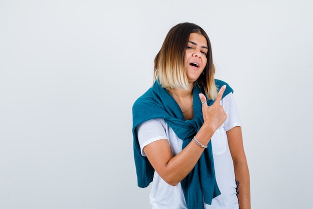 Young woman pointing up in white t-shirt and looking pleased , front view.