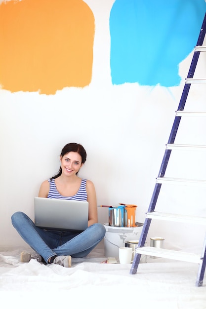 Young woman portrait while painting new apartment sitting with laptop Young woman with laptop