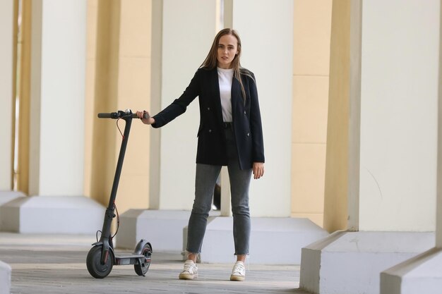 A young woman poses near an electric scooter in the cityModern transport for movement in the metropolis