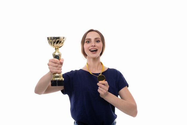 A young woman poses with the winner's cup and gold medal on a white background