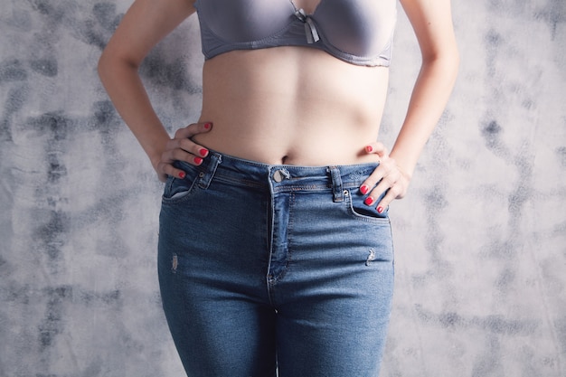 Young woman posing in jeans and bras on gray