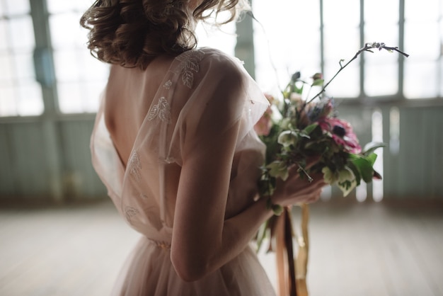 Young woman posing in a pink long dress backs indoors