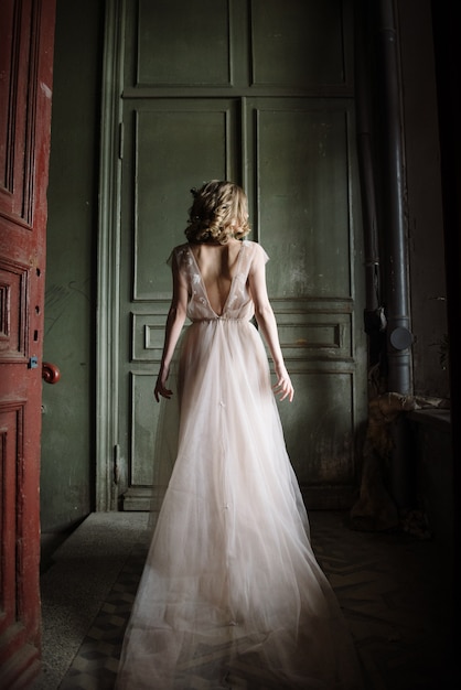 Young woman posing in a pink long dress backs indoors