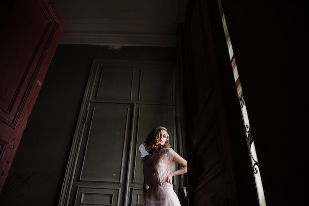 Young woman posing in a pink tender light long dress indoors