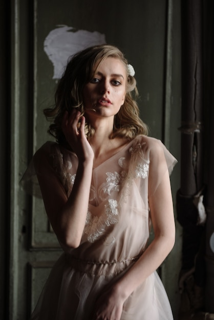 Young woman posing in a pink tender light long dress indoors