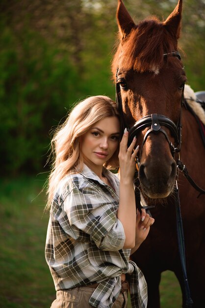 Young woman posing with a brown horse in a forest in a sunny meadow.