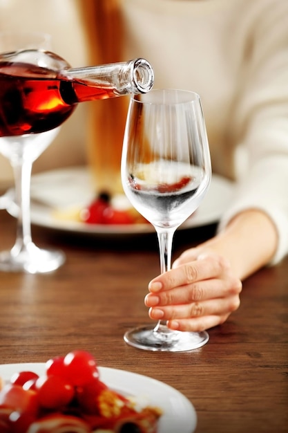 Young woman pouring pink wine into glass on the table