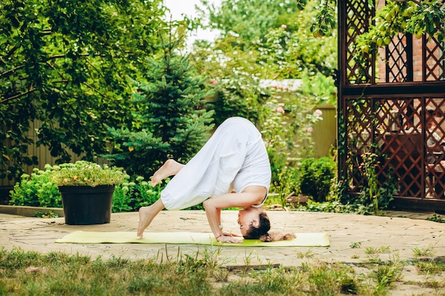 Young woman practices yoga in courtyard of a country house Headstand Ardha Salamba Shirshasana