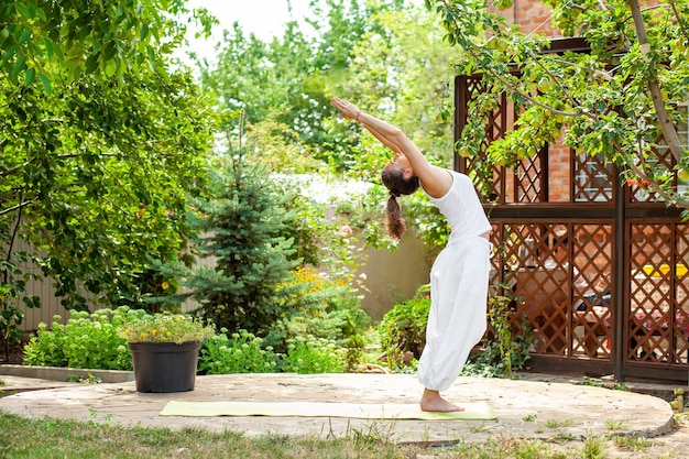 Young woman practices yoga in the garden Deflection in the practice of surya namaskar Tadasana Mountain pose with stretched hands