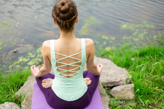 Young woman practices yoga near a river