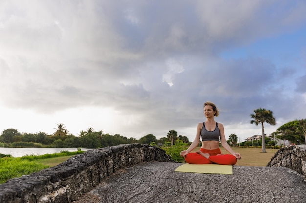 A young woman practices yoga on the ocean coast during sunrise