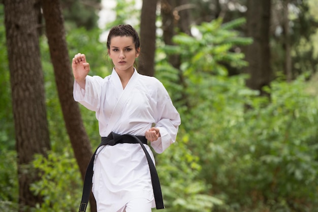 Young Woman Practicing Her Karate Moves in Wooded Forest Area  White Kimono  Black Belt