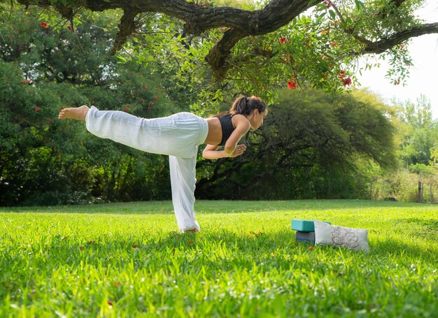 Young Woman Practicing Yoga Doing Warrior 2 Pose Under a Tree in a ParkWellness Concept