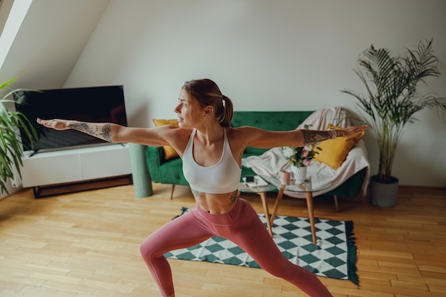 Young woman practicing yoga in a living room with houseplants and wooden flooring