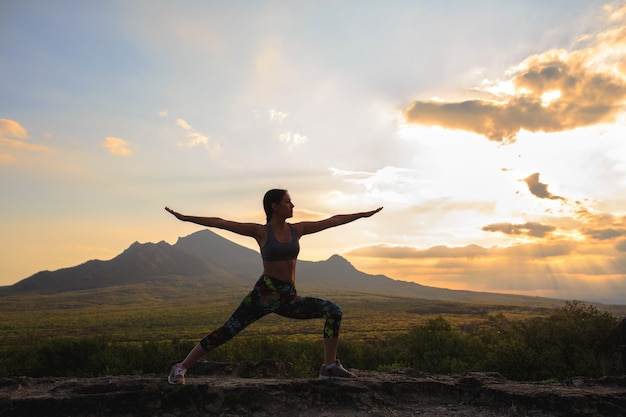 Young woman practicing yoga at sunset in beautiful mountain location.