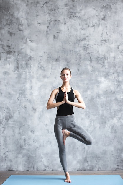 Young woman practicing yoga vrikshasana in gym