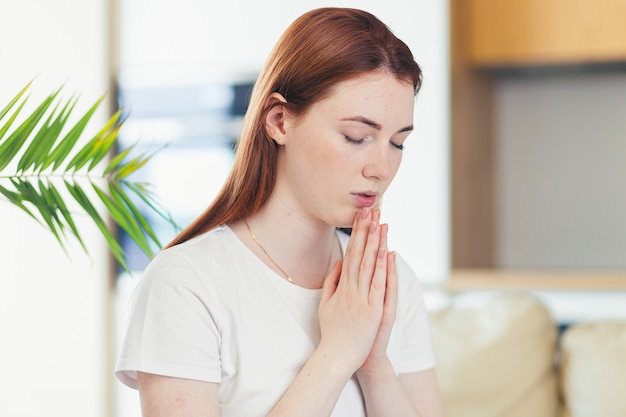  young woman praying sincerely with folded arms at home 