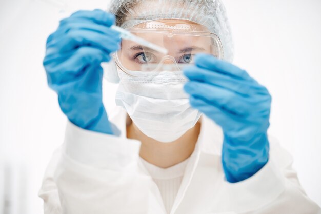 Young woman in protective gloves making coronavirus test with special reagent in laboratory