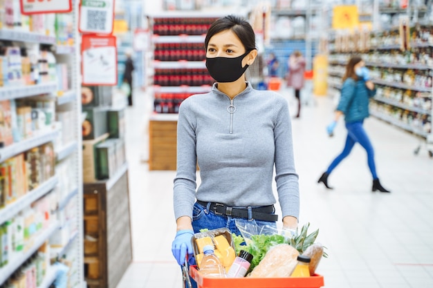 Young woman in protective mask and gloves choosing products in the supermarket. Safe shopping during a pandemic.