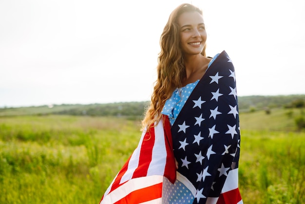 Young woman proudly hold waving american USA flag on blooming meadow 4th of July Independence Day