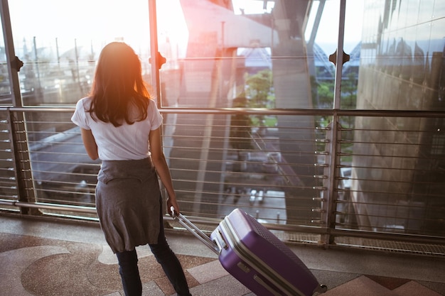 Young woman pulling suitcase in  airport terminal. Copy space