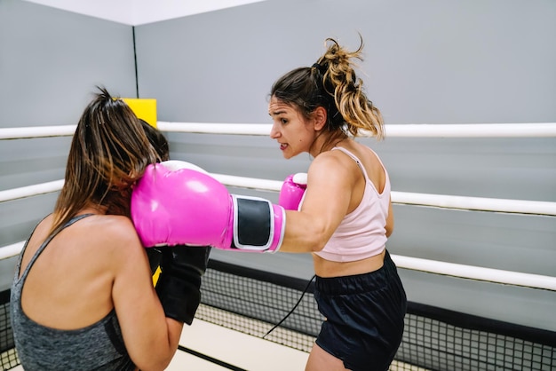 A young woman punching her partner in the side of the head in a boxing practice in the ring